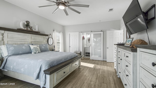 bedroom featuring a barn door, visible vents, ceiling fan, and wood finished floors