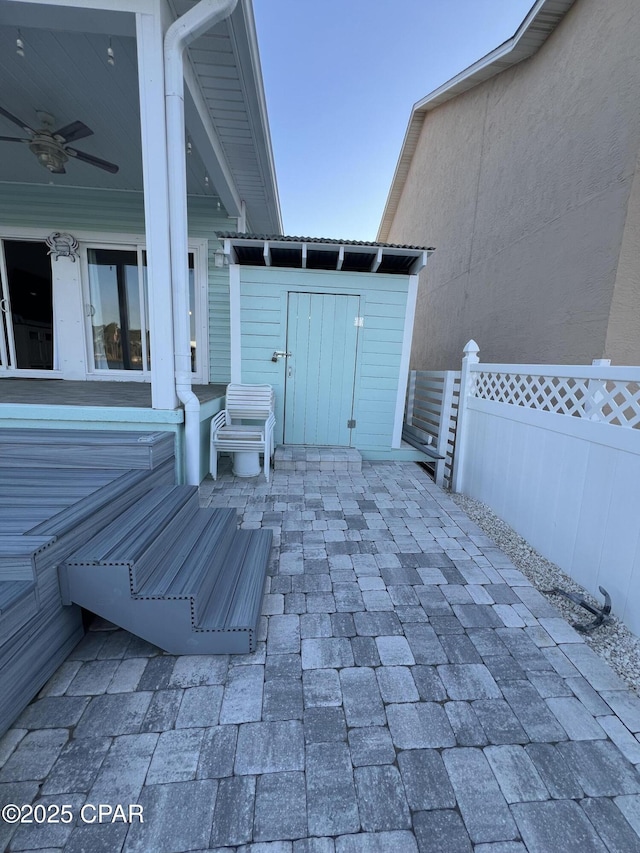 view of patio / terrace with a ceiling fan, an outdoor structure, fence, and a storage unit