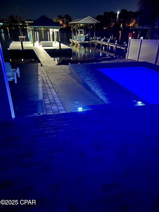 pool at night with a boat dock, a water view, and a gazebo