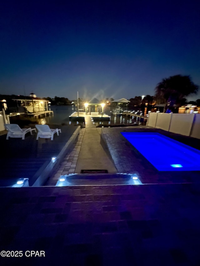 pool at twilight with a water view, fence, and a fenced in pool