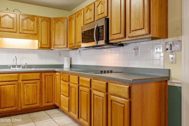 kitchen featuring light tile patterned floors, decorative backsplash, stainless steel microwave, black electric stovetop, and a sink