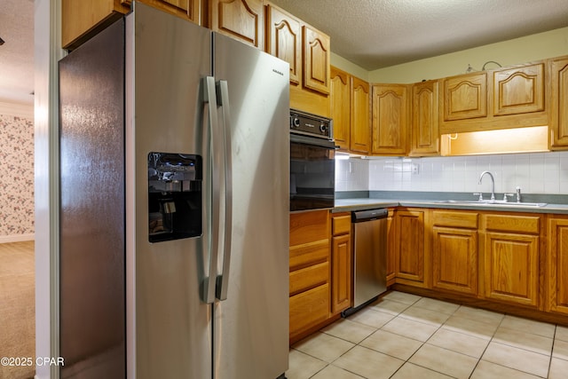 kitchen with a textured ceiling, stainless steel appliances, a sink, tasteful backsplash, and wallpapered walls