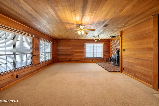 unfurnished living room with visible vents, wooden ceiling, a wood stove, carpet floors, and wood walls