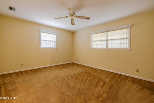 carpeted spare room with visible vents, baseboards, and a ceiling fan