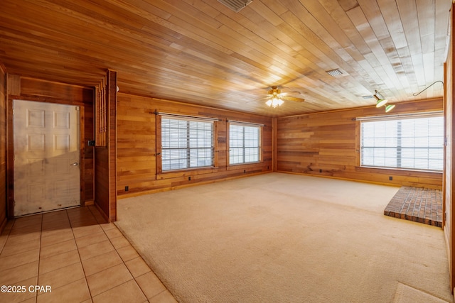 unfurnished living room featuring a healthy amount of sunlight, wooden walls, light tile patterned flooring, and light colored carpet