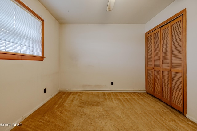 unfurnished bedroom featuring light carpet, ceiling fan, a closet, and baseboards