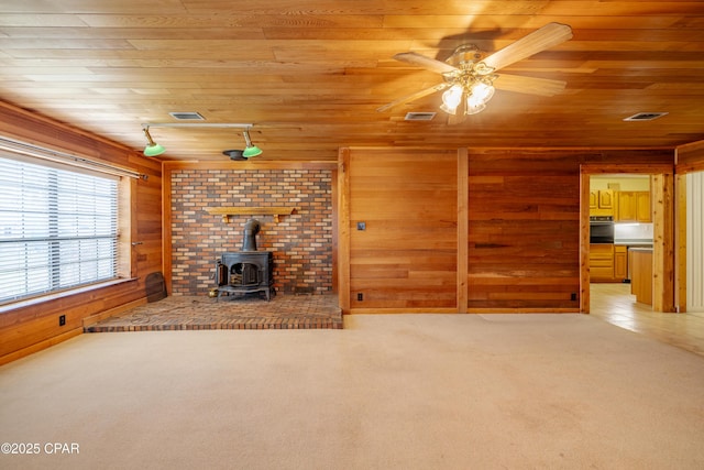 unfurnished living room with a wood stove, light carpet, and wooden ceiling