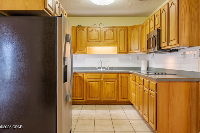 kitchen featuring brown cabinets, light tile patterned floors, stainless steel appliances, backsplash, and a sink