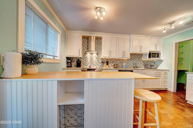 kitchen with wall chimney exhaust hood, appliances with stainless steel finishes, a breakfast bar area, and white cabinetry