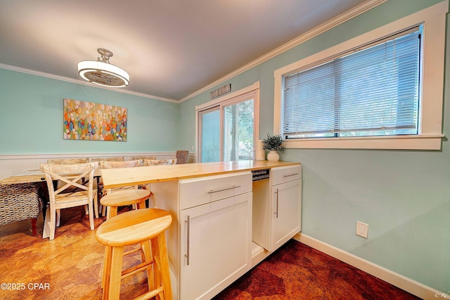 kitchen with baseboards, wainscoting, butcher block counters, ornamental molding, and white cabinetry