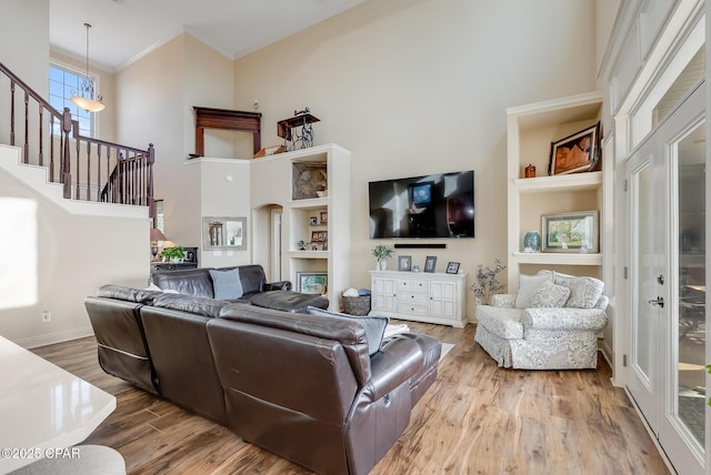 living room with a towering ceiling, stairway, ornamental molding, wood finished floors, and a chandelier