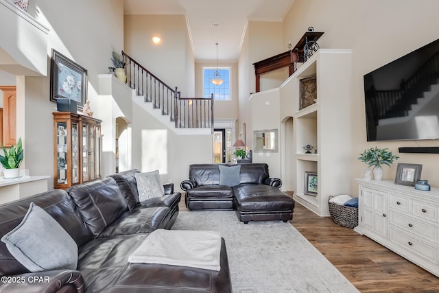 living area featuring built in features, arched walkways, a towering ceiling, stairway, and dark wood-style flooring