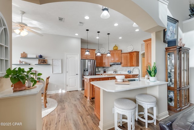 kitchen with a peninsula, a sink, a kitchen island, light countertops, and stainless steel fridge with ice dispenser