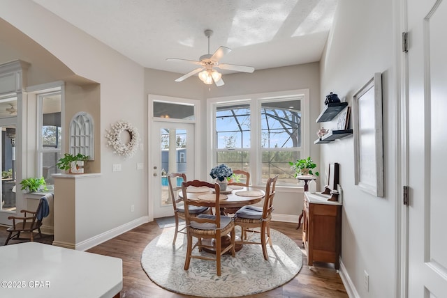 dining space with ceiling fan, a textured ceiling, baseboards, and wood finished floors