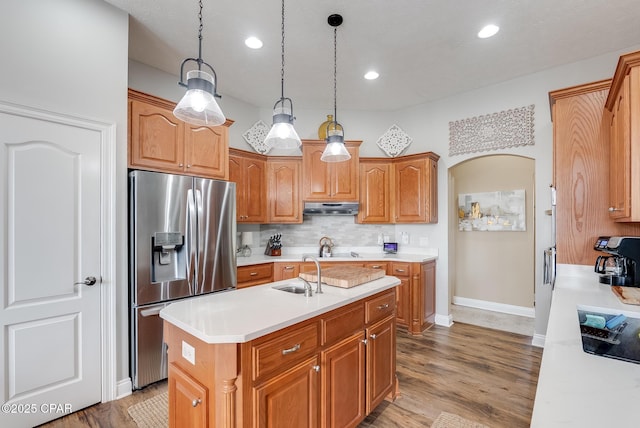 kitchen featuring arched walkways, light countertops, a sink, stainless steel fridge, and under cabinet range hood