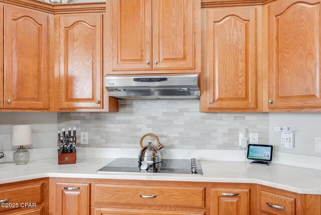 kitchen featuring light countertops, tasteful backsplash, black electric cooktop, and under cabinet range hood