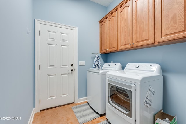 clothes washing area featuring washing machine and dryer, cabinet space, and baseboards