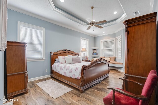 bedroom featuring ornamental molding, a tray ceiling, wood finished floors, and visible vents