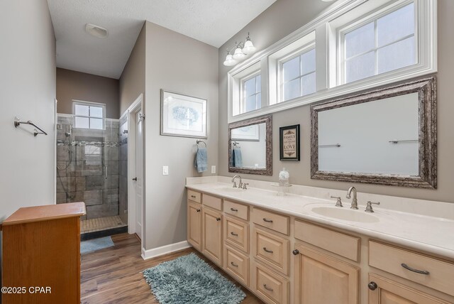 full bath with double vanity, wood finished floors, a sink, and tiled shower