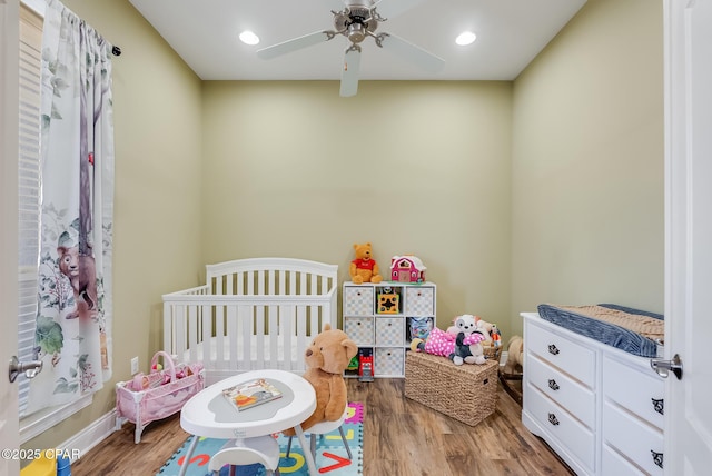 bedroom with a ceiling fan, recessed lighting, a crib, and wood finished floors