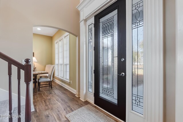 foyer featuring baseboards, stairs, arched walkways, and wood finished floors