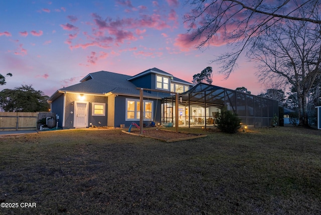 rear view of house with a yard, stucco siding, a lanai, and fence