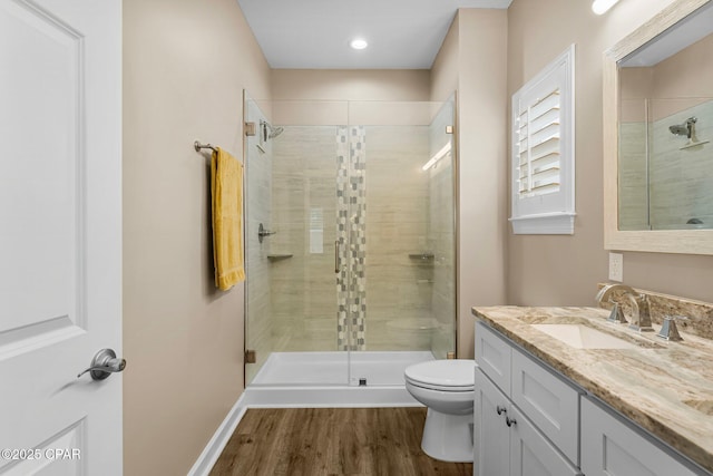 full bath featuring toilet, vanity, a shower stall, wood finished floors, and baseboards