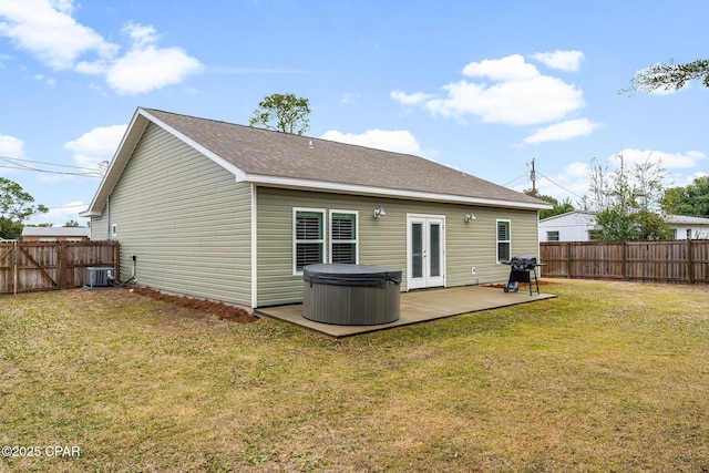 rear view of property with french doors, roof with shingles, a lawn, a hot tub, and a fenced backyard