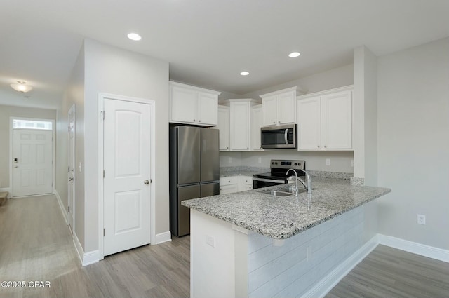 kitchen featuring light stone counters, light wood-style flooring, stainless steel appliances, a peninsula, and white cabinets