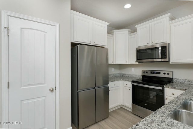 kitchen with stainless steel appliances, white cabinets, light wood finished floors, and light stone countertops