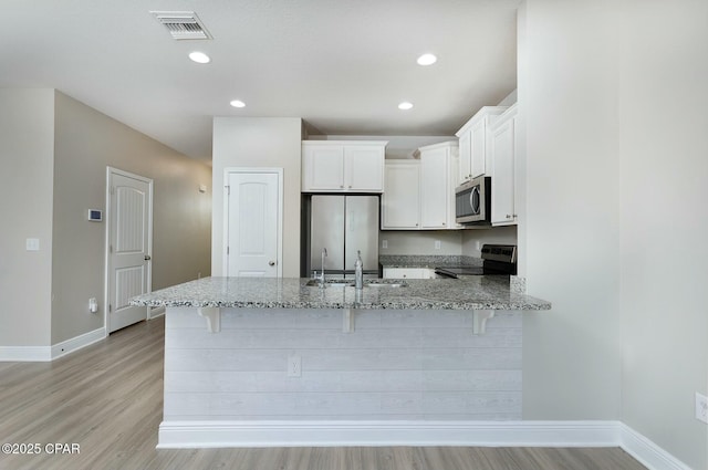 kitchen featuring light stone counters, visible vents, appliances with stainless steel finishes, a sink, and a peninsula