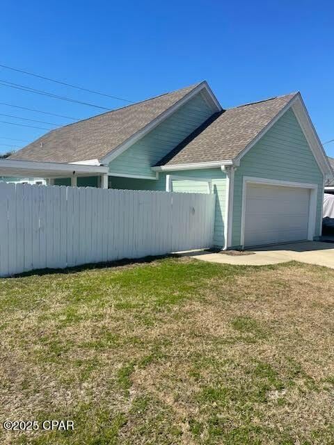 view of home's exterior with driveway, a shingled roof, an attached garage, fence, and a yard