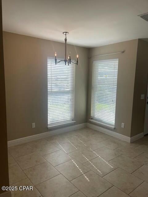 spare room featuring a chandelier, baseboards, and a healthy amount of sunlight