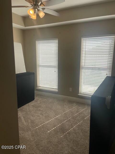 carpeted spare room featuring baseboards, a tray ceiling, and a ceiling fan