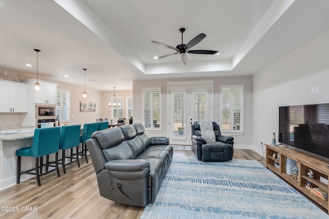 living room with light wood-type flooring, a raised ceiling, recessed lighting, and ceiling fan with notable chandelier