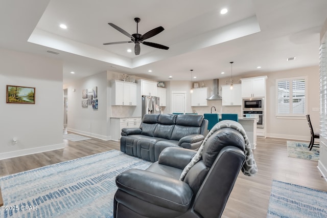 living area featuring light wood-style flooring, a tray ceiling, baseboards, and recessed lighting