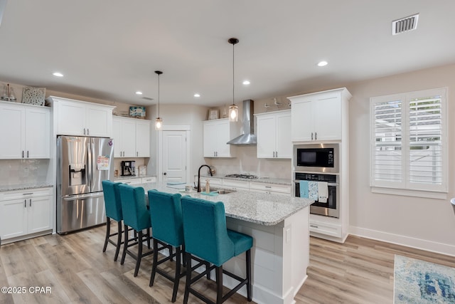 kitchen featuring decorative backsplash, light wood-style floors, stainless steel appliances, wall chimney range hood, and a sink