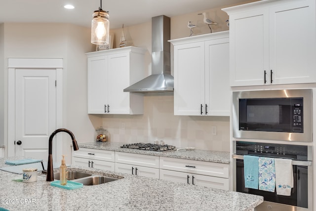 kitchen with appliances with stainless steel finishes, wall chimney range hood, white cabinetry, pendant lighting, and a sink