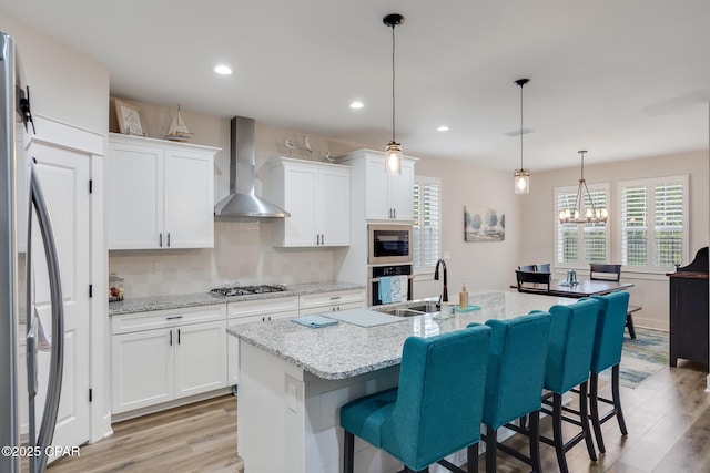 kitchen with light wood finished floors, wall chimney exhaust hood, appliances with stainless steel finishes, and a sink