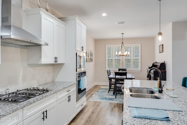 kitchen featuring a sink, wall chimney range hood, appliances with stainless steel finishes, light wood-type flooring, and decorative backsplash