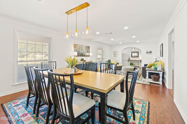 dining room with arched walkways, recessed lighting, ornamental molding, wood finished floors, and baseboards