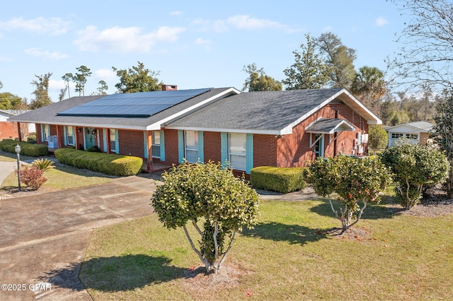 ranch-style home featuring a shingled roof, roof mounted solar panels, brick siding, and a front lawn