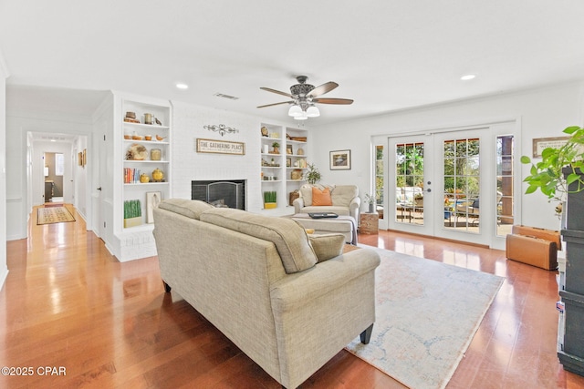 living area featuring visible vents, light wood-style flooring, french doors, a brick fireplace, and built in shelves