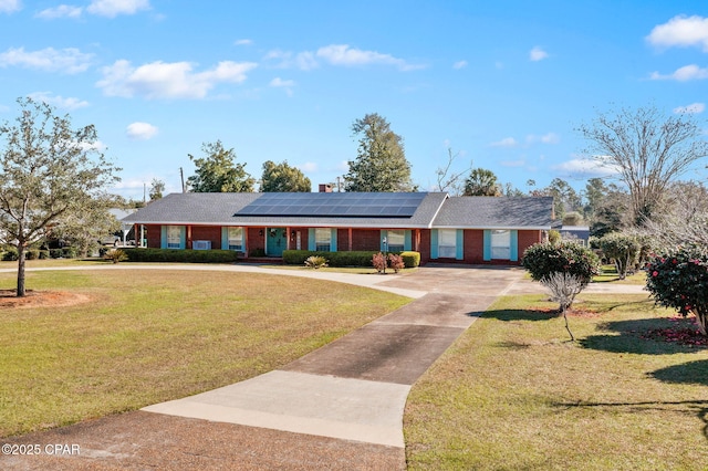 ranch-style home with driveway, a front lawn, brick siding, and roof mounted solar panels