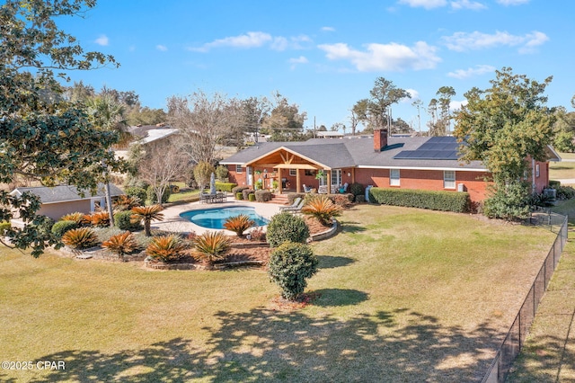 rear view of property featuring an outdoor pool, a patio, fence, a yard, and roof mounted solar panels