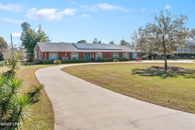 view of front of home with brick siding, driveway, a front lawn, and solar panels