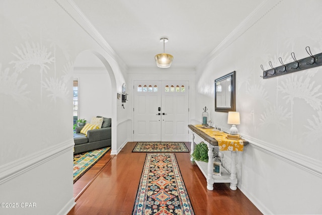 entryway featuring baseboards, ornamental molding, arched walkways, and wood finished floors