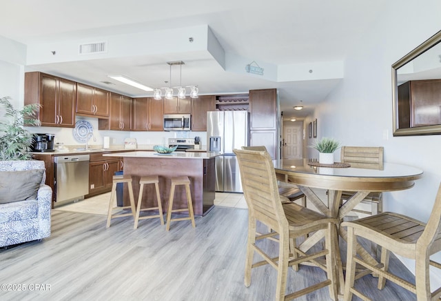 kitchen with a kitchen island, a breakfast bar area, light wood-type flooring, light countertops, and appliances with stainless steel finishes