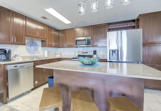 kitchen with visible vents, light tile patterned flooring, a kitchen breakfast bar, a sink, and appliances with stainless steel finishes