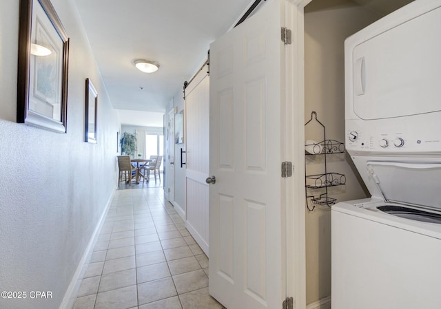 laundry room featuring stacked washer and dryer, laundry area, a barn door, baseboards, and light tile patterned floors